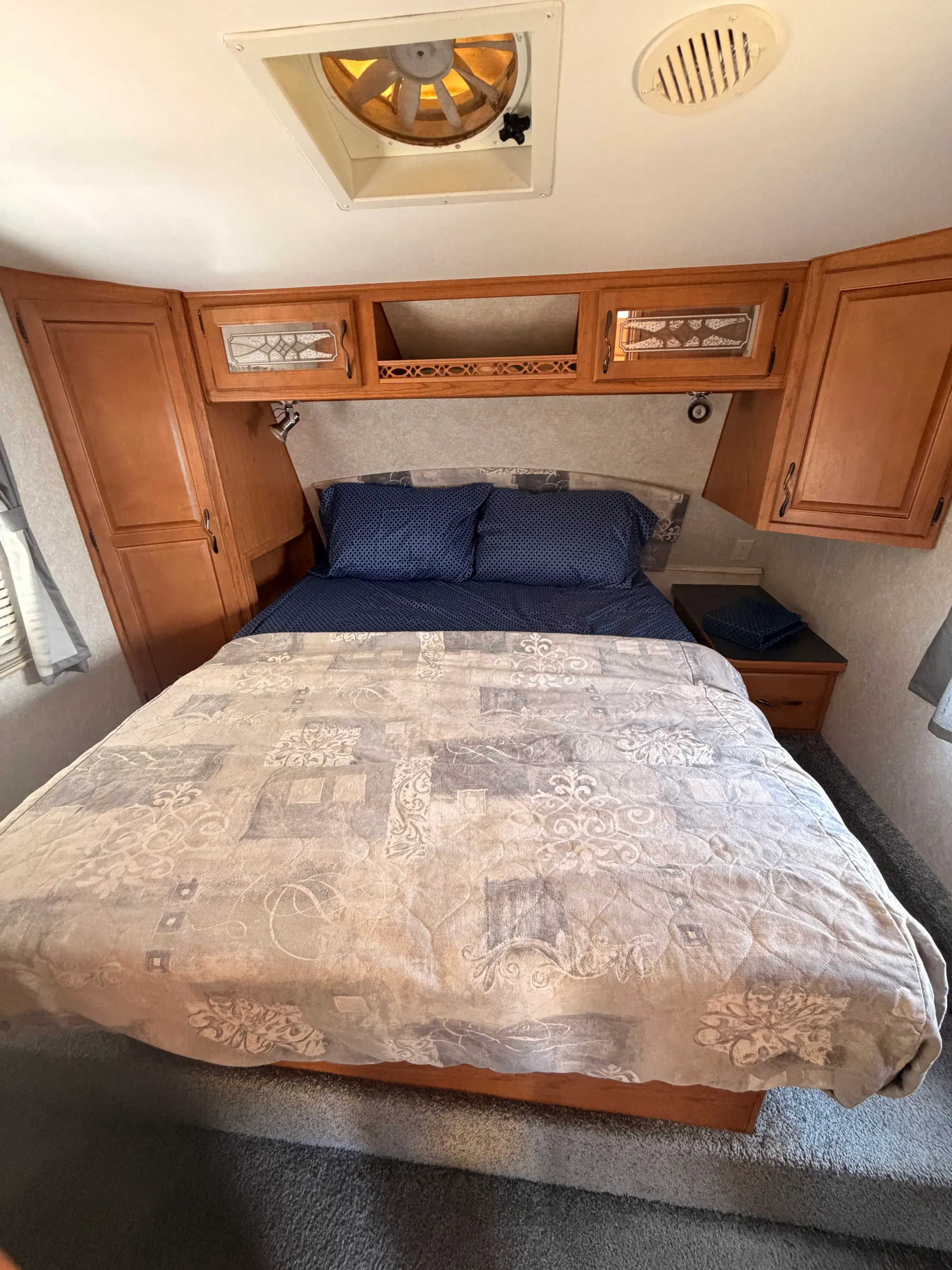 Private front bedroom with a made-up queen bed, wardrobe cabinets and a roof vent fan