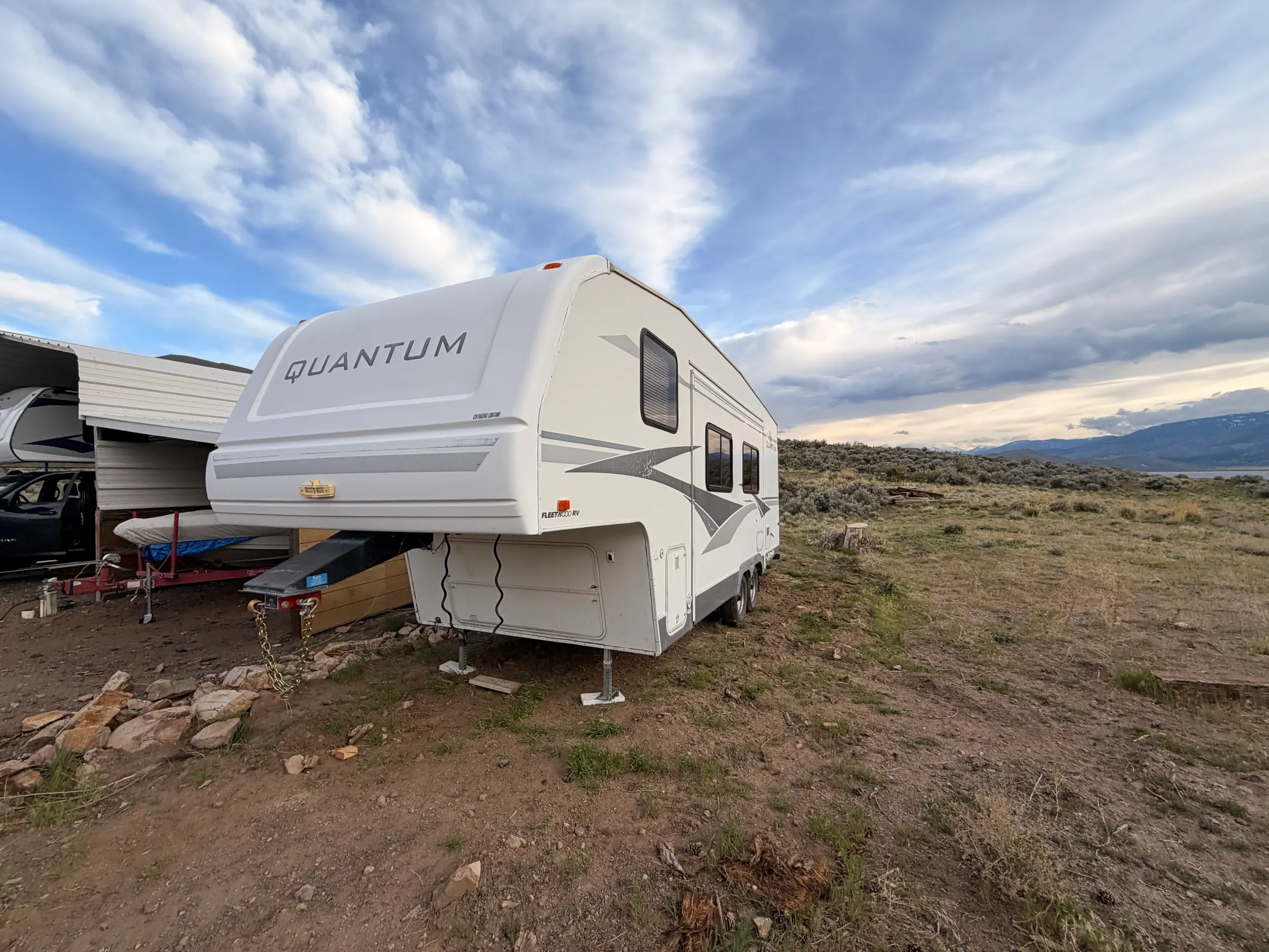 The Fleetwood Terry Quantum fifth wheel parked on open high desert at dusk, front cap and mountains behind it